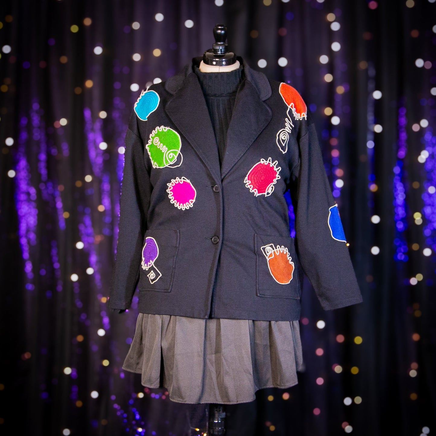 Black blazer with colorful patches on a mannequin against a sparkling curtain background